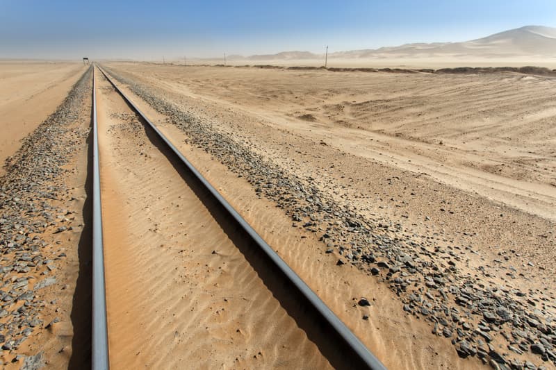 Ein Bahngleis führt durch den Sand der Namib, am Horizont liegen Dünen