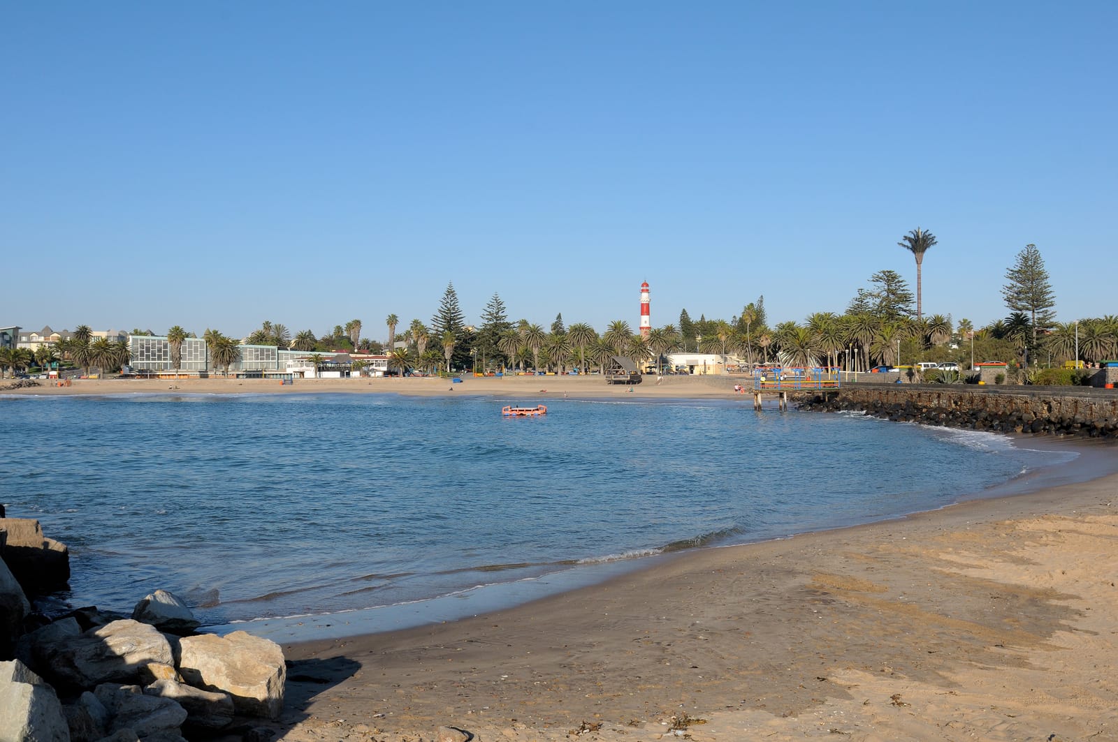 Kleine Badebucht an der Mole in Swakopmund mit Palmen, in der Ferne der Leuchtturm