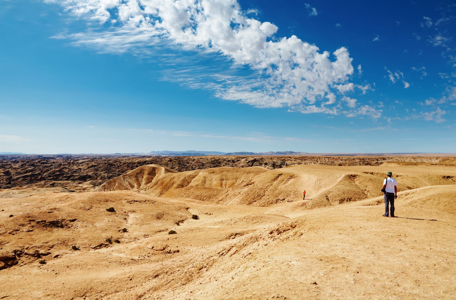 Zerfurchte, kahle Erosionslandschaft unter Wolken, auf einem Kamm ein Wanderer