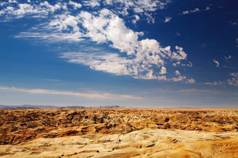Weite, zerfurchte Erosionslandschaft unter dramatischem Wolkenhimmel