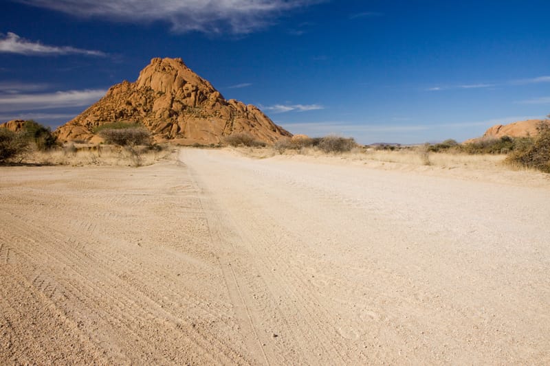 Schotterpiste, dahinter der Granitgipfel der Spitzkoppe